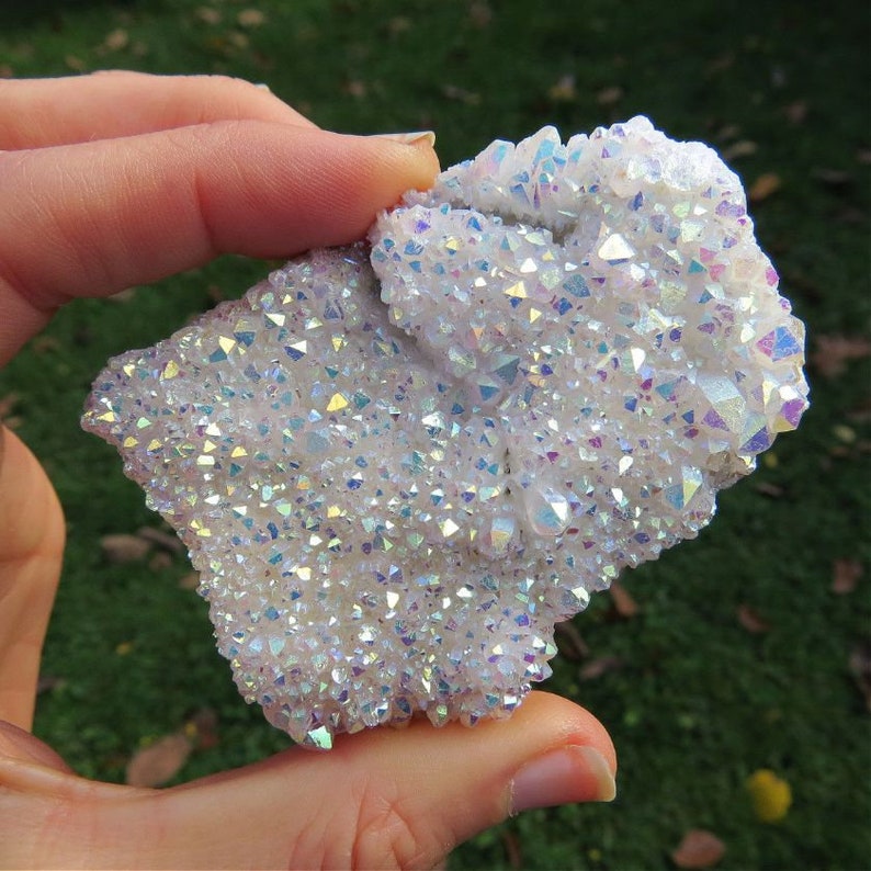 Puede incluir: Un c&uacute;mulo de cristales de cuarzo blanco iridiscente con un brillo arco&iacute;ris. Los cristales est&aacute;n densamente empaquetados, creando una exhibici&oacute;n &uacute;nica y hermosa.