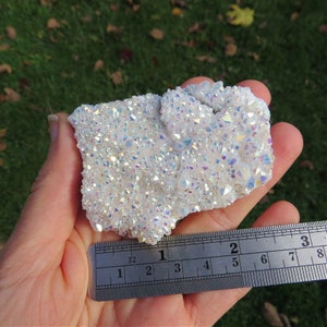 Puede incluir: Un c&uacute;mulo de cristales blancos e iridiscentes con un brillo arco&iacute;ris. El c&uacute;mulo mide aproximadamente 5 cm de ancho y 7,5 cm de largo.