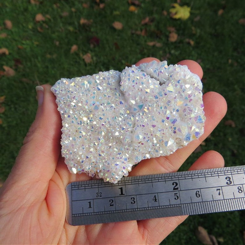 Puede incluir: Un c&uacute;mulo de cristales blancos e iridiscentes con un brillo arco&iacute;ris. El c&uacute;mulo mide aproximadamente 5 cm de ancho y 7,5 cm de largo.