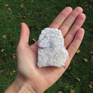 Puede incluir: Un c&uacute;mulo de cristales blancos iridiscentes con una textura rugosa y natural. El cristal mide aproximadamente 12,5 cm de largo y 10 cm de ancho.