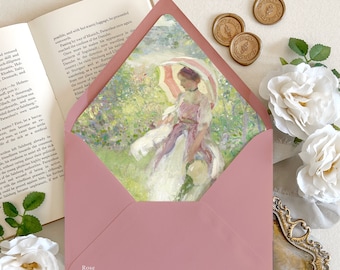 May include: A dusty rose envelope with a pointed flap featuring an impressionist painting of a person with a parasol in a garden. The envelope is displayed alongside an open book, two gold wax seals, white roses, and a small ornate gold frame.