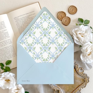 May include: An open book and a light blue envelope with a floral patterned interior are displayed with white roses and gold wax seals. The envelope has the words "Azure Blue" printed on it.