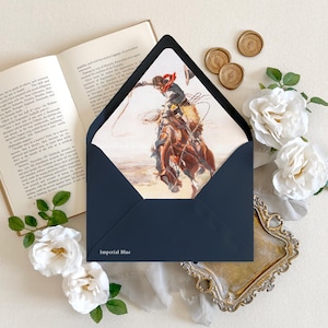 Op de afbeelding: Een donkerblauwe envelop met de tekst Imperial Blue gedrukt op de onderste flap. De voering van de envelop bevat een gedetailleerde illustratie van een cowboy die op een bokkend paard rijdt terwijl hij met een lasso zwaait.