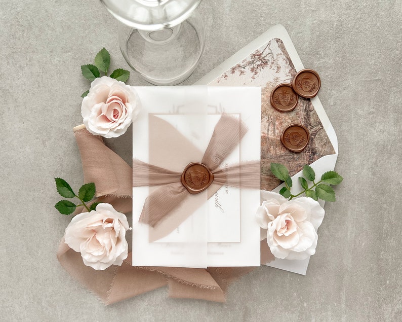 May include: A set of white and cream wedding invitations with a brown ribbon and wax seal. The invitations are decorated with delicate pink roses and greenery.