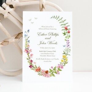 May include: A white wedding rehearsal dinner invitation with a floral wreath border. The invitation reads "Please join us for a Rehearsal Dinner honoring Esther Phillips and John Woods. Friday, June 26 at 6pm Ruth Lake Country Club 6200 Madison Street Hinsdale, Illinois 60521 Kindly Reply by June 12 to Claudia 123.456.7890"