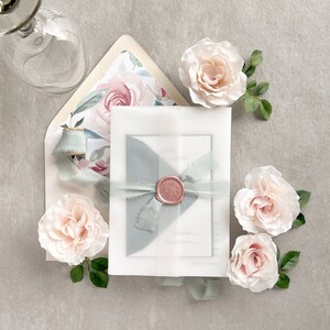 May include: A white envelope with a blue and pink floral pattern, tied with a blue ribbon and a wax seal. The envelope is surrounded by pink roses.