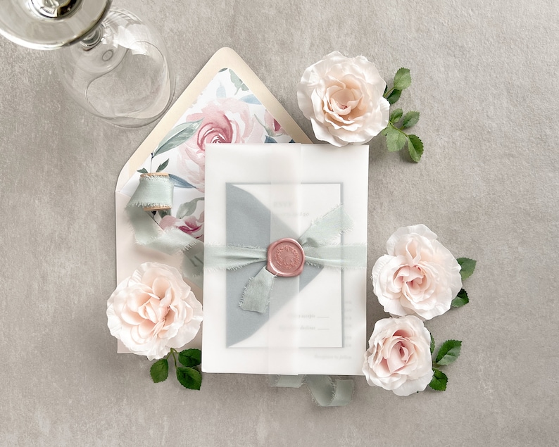 May include: A white envelope with a blue and pink floral pattern, tied with a blue ribbon and a wax seal. The envelope is surrounded by pink roses.