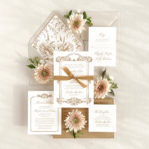 May include: Wedding invitation suite with gold accents and floral embellishments. The invitation features a gold ornate frame with the text "Mr. and Mrs. Thomas Lawson request the pleasure of your company at the wedding of Caroline Rose and Glenn The Donnelly House Birmingham, Alabama August 26, 2023 at 6:30 pm.  Reception to follow at the same location."