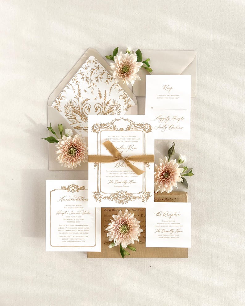 May include: Wedding invitation suite with gold accents and floral embellishments. The invitation features a gold ornate frame with the text "Mr. and Mrs. Thomas Lawson request the pleasure of your company at the wedding of Caroline Rose and Glenn The Donnelly House Birmingham, Alabama August 26, 2023 at 6:30 pm.  Reception to follow at the same location."