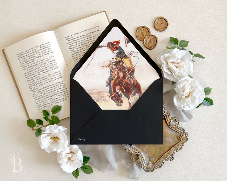 Op de afbeelding: Een zwarte envelop met het woord Ebony op de voorzijde, met een illustratie van een cowboy op een bokkend bruin paard die een lasso vasthoudt. De envelop is omringd door een open boek, witte rozen en gouden waszegels.