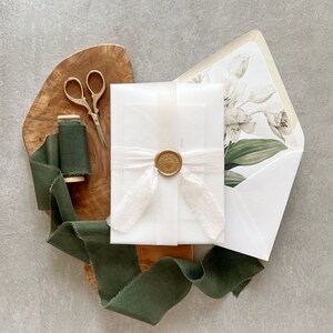 May include: A white envelope with a wax seal and a green ribbon. The envelope is on a wooden surface with a spool of green ribbon and a pair of silver scissors.
