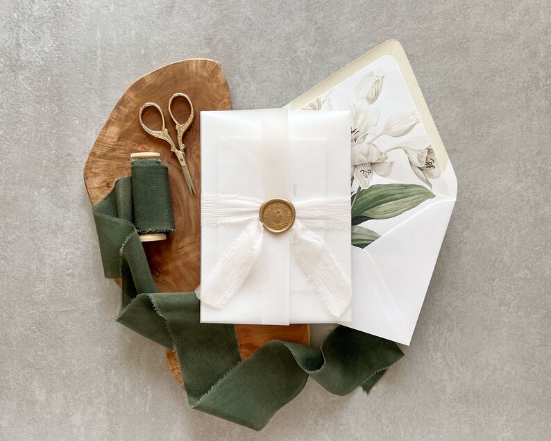 May include: A white envelope with a wax seal and a green ribbon. The envelope is on a wooden surface with a spool of green ribbon and a pair of silver scissors.