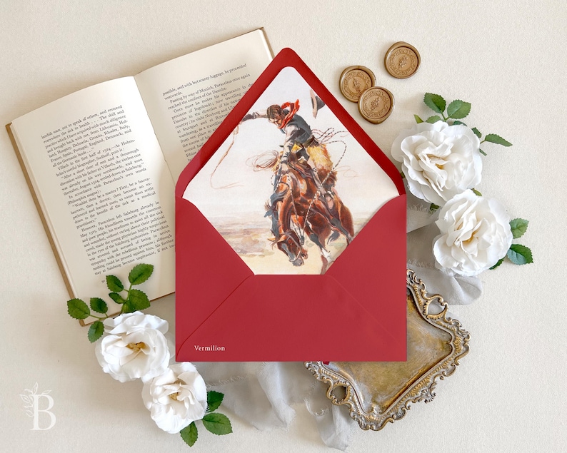 Op de afbeelding: Een dieprode envelop met een puntige klep, voorzien van een binnenvoering bedrukt met een aquarelillustratie van een cowboy op een bokkend paard. Het woord Vermilion is in het wit gedrukt in de linkerbenedenhoek van de envelop.