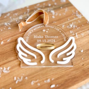 Wood or frosted acrylic baby memorial ornament.  Features matte white acrylic wings and a gold halo.  Personalize with baby's name and date.  Includes khaki velvet ribbon for hanging.