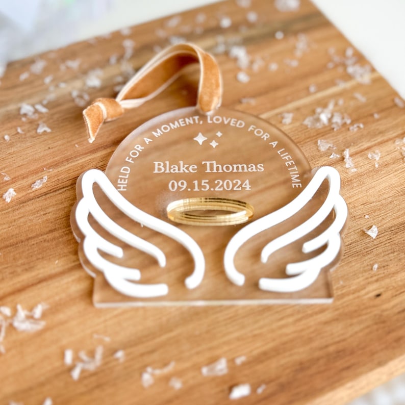 Wood or frosted acrylic baby memorial ornament.  Features matte white acrylic wings and a gold halo.  Personalize with baby's name and date.  Includes khaki velvet ribbon for hanging.