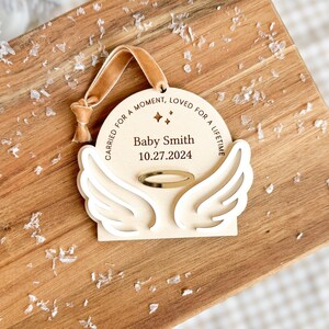 Wood or frosted acrylic baby memorial ornament.  Features matte white acrylic wings and a gold halo.  Personalize with baby's name and date.  Includes khaki velvet ribbon for hanging.