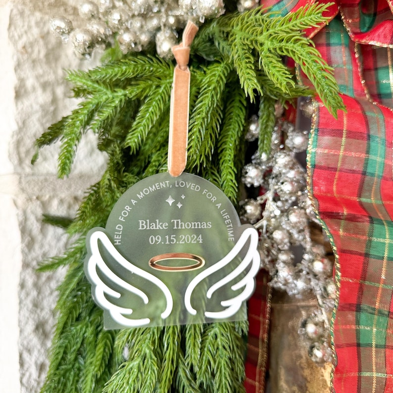 Wood or frosted acrylic baby memorial ornament.  Features matte white acrylic wings and a gold halo.  Personalize with baby's name and date.  Includes khaki velvet ribbon for hanging.