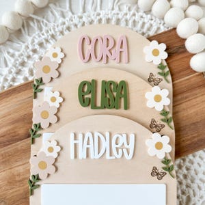 First/Last day of school sign with acrylic flowers and engraved butterflies. Features child's name in choice of acrylic color, and white areas to write milestones with a dry erase marker (not included).