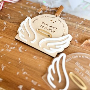 Wood or frosted acrylic baby memorial ornament.  Features matte white acrylic wings and a gold halo.  Personalize with baby's name and date.  Includes khaki velvet ribbon for hanging.