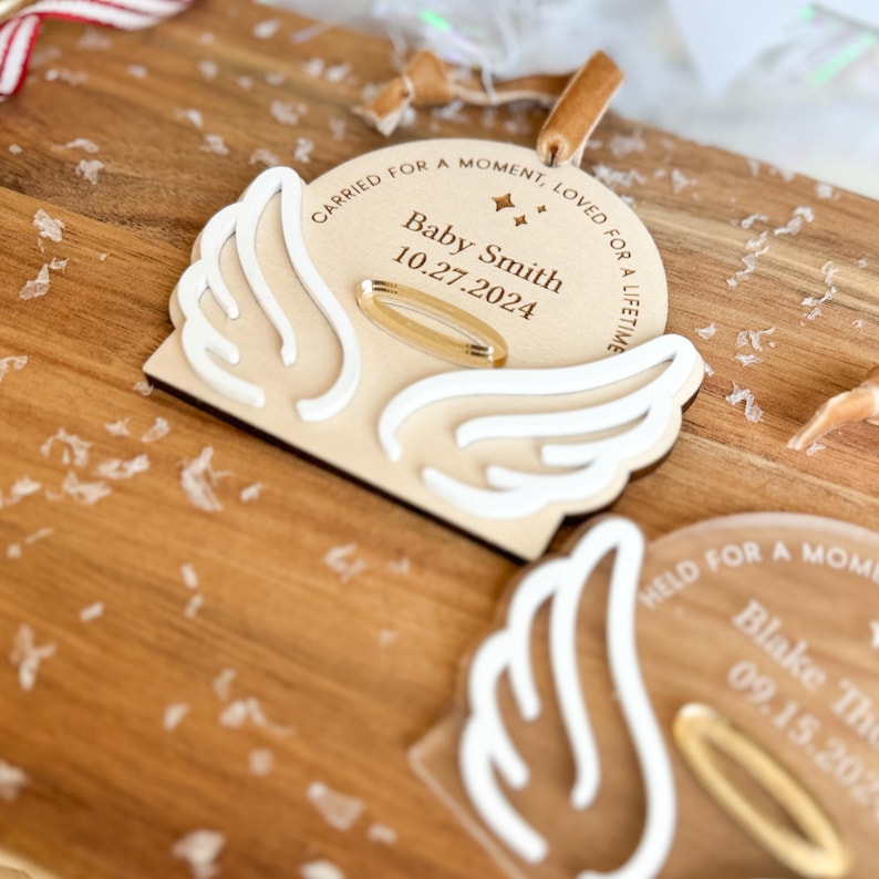 Wood or frosted acrylic baby memorial ornament.  Features matte white acrylic wings and a gold halo.  Personalize with baby's name and date.  Includes khaki velvet ribbon for hanging.
