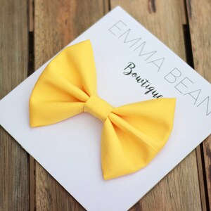 May include: A bright yellow fabric bow on a white card with the text "Emma Bean Boutique".