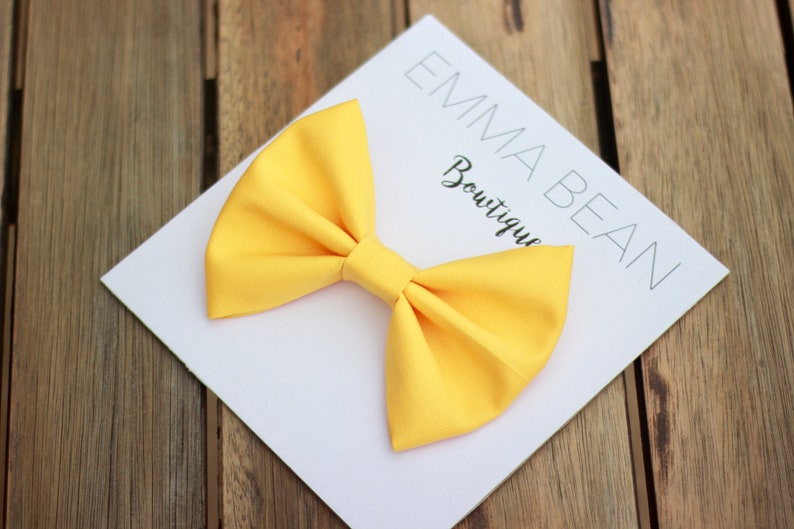 May include: A bright yellow fabric bow on a white card with the text "Emma Bean Boutique".