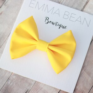 May include: A bright yellow bow tie on a white card with the text "Emma Bean Boutique".