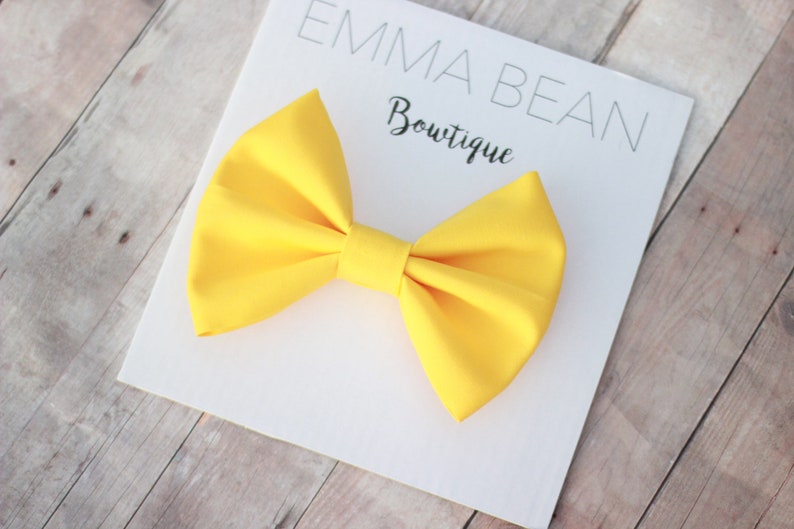 May include: A bright yellow bow tie on a white card with the text "Emma Bean Boutique".