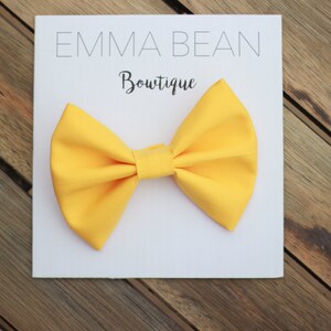 May include: A bright yellow bow tie on a white card with the text "Emma Bean Boutique".