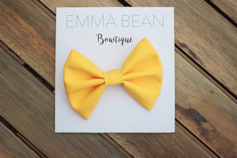 May include: A bright yellow bow tie on a white card with the text "Emma Bean Boutique".