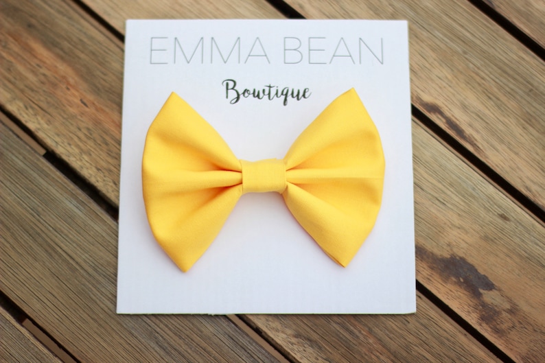May include: A yellow bow tie on a white background with the text "Emma Bean Boutique".
