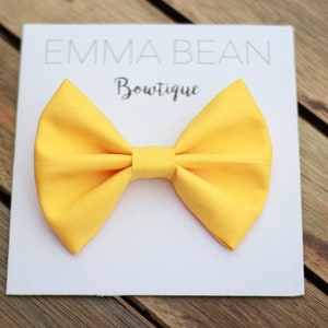 May include: A yellow bow tie on a white card with the text "Emma Bean Boutique".