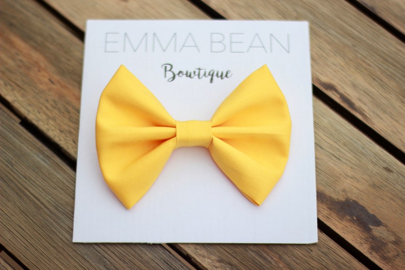 May include: A yellow bow tie on a white card with the text "Emma Bean Boutique".