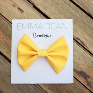May include: A yellow bow tie on a white card with the text "Emma Bean Boutique".