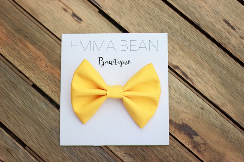 May include: A yellow bow tie on a white card with the text "Emma Bean Boutique".