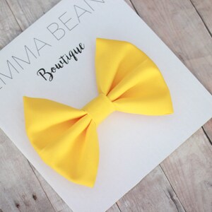May include: A large, bright yellow bow on a white card with the text "Emma Bean Boutique".