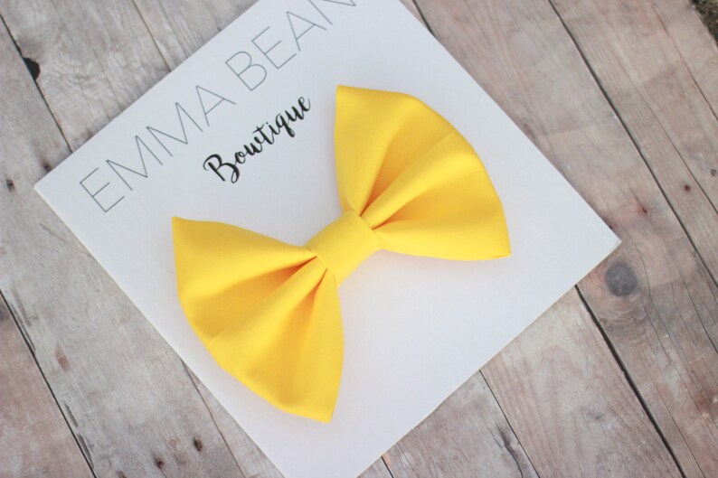 May include: A large, bright yellow bow on a white card with the text "Emma Bean Boutique".