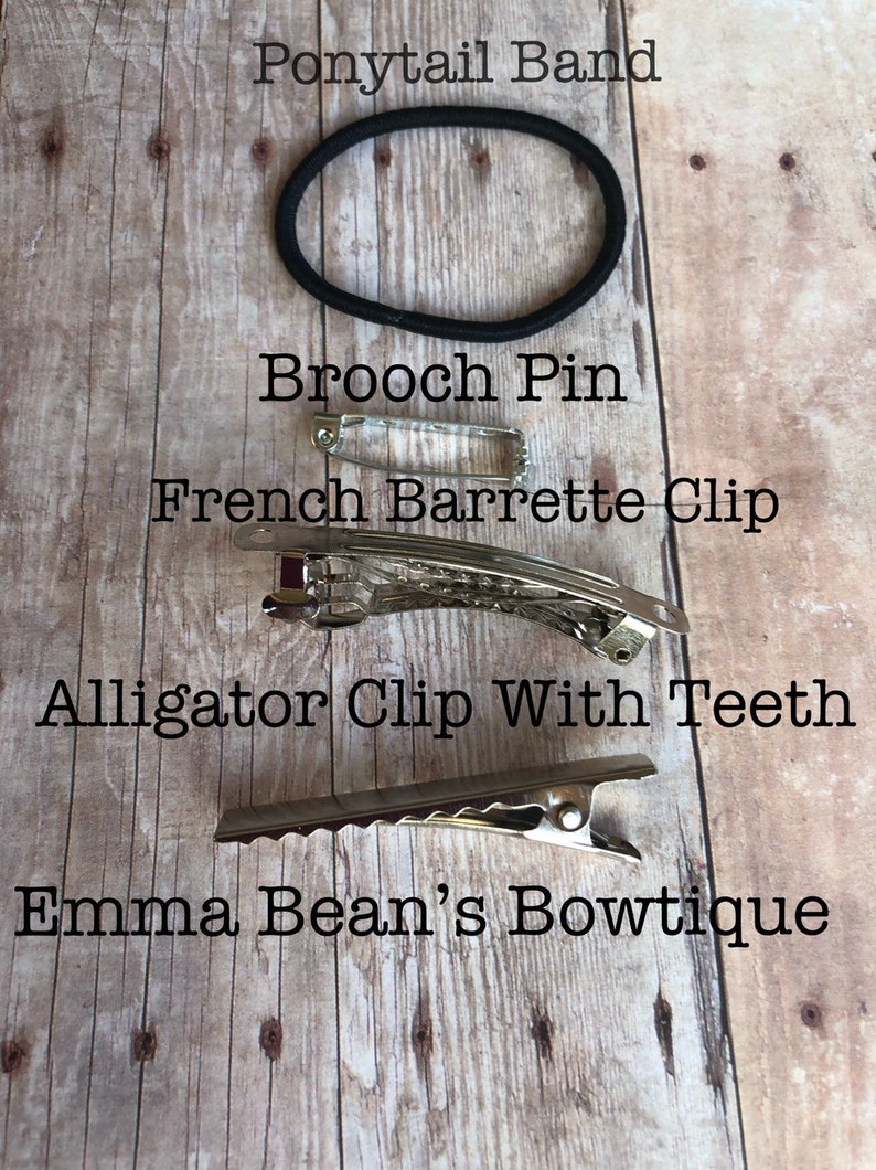 May include: A close-up of four different hair accessories on a wooden surface. The accessories include a ponytail band, a brooch pin, a French barrette clip, and an alligator clip with teeth. The text "Emma Bean's Bowtique" is visible at the bottom of the image.