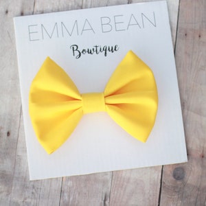 May include: A bright yellow bow tie on a white card with the text "Emma Bean Boutique".