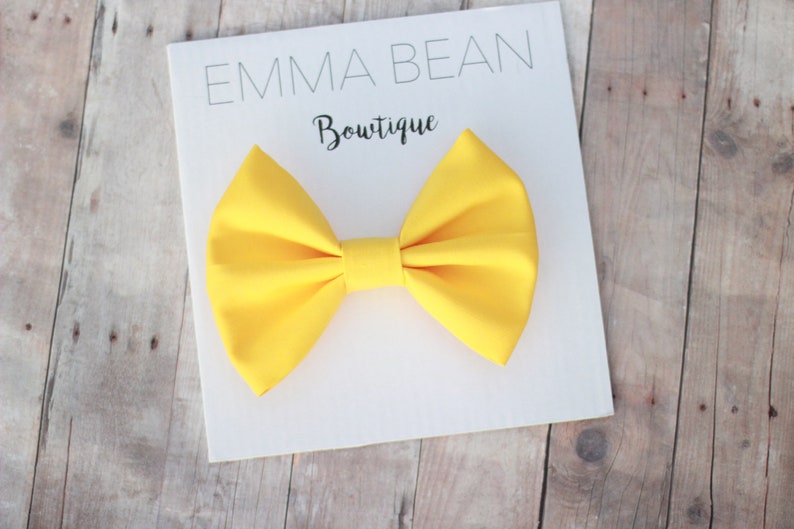 May include: A bright yellow bow tie on a white card with the text "Emma Bean Boutique".
