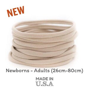 May include: A stack of 20 nude elastic hair ties, made in the USA. The hair ties are suitable for newborns to adults, with a size range of 26cm to 80cm.