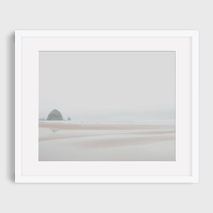 May include: A framed photograph of a rocky island in the distance, with a sandy beach in the foreground. The sky and water are a muted gray, creating a serene and minimalist aesthetic.