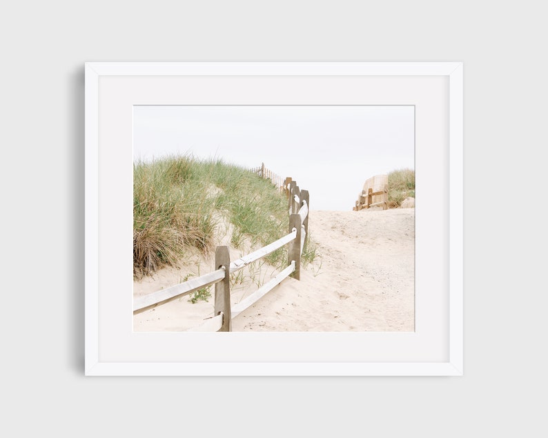 May include: A wooden fence leads up a sandy path through tall grass to a beach.