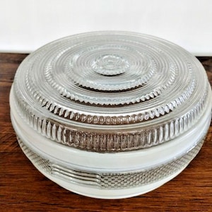 May include: A clear glass light fixture cover with a circular, ridged design. The cover has a white band around the middle and a textured bottom. The fixture is likely for a ceiling light or pendant.