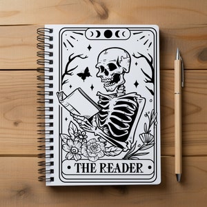 May include: A black and white illustration of a skeleton reading a book. The illustration is in the style of a tarot card and features the text "The Reader".