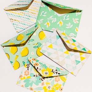 May include: Five different patterned envelopes with a green background and yellow accents. The patterns include lemons, flowers, birds, and geometric shapes.