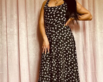 May include: A black sleeveless midi dress with a white floral print. The dress has a scoop neckline and a fitted bodice. The skirt is full and flows out from the waist.