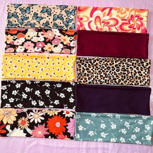 Op de afbeelding: Tien verschillende stoffen hoofdbanden met verschillende patronen, waaronder vlinders, bloemen en dierenprint. De hoofdbanden zijn allemaal in verschillende kleuren, waaronder geel, rood, blauw, groen en zwart.