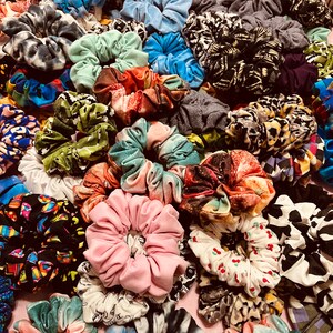 May include: A collection of colorful fabric scrunchies in various patterns and designs. The scrunchies are made of different materials, including cotton, silk, and velvet. They are arranged in a random order, creating a visually appealing display.