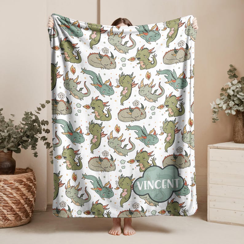 A person is holding a blanket with a repeating pattern of green and orange cartoon-style dragons.